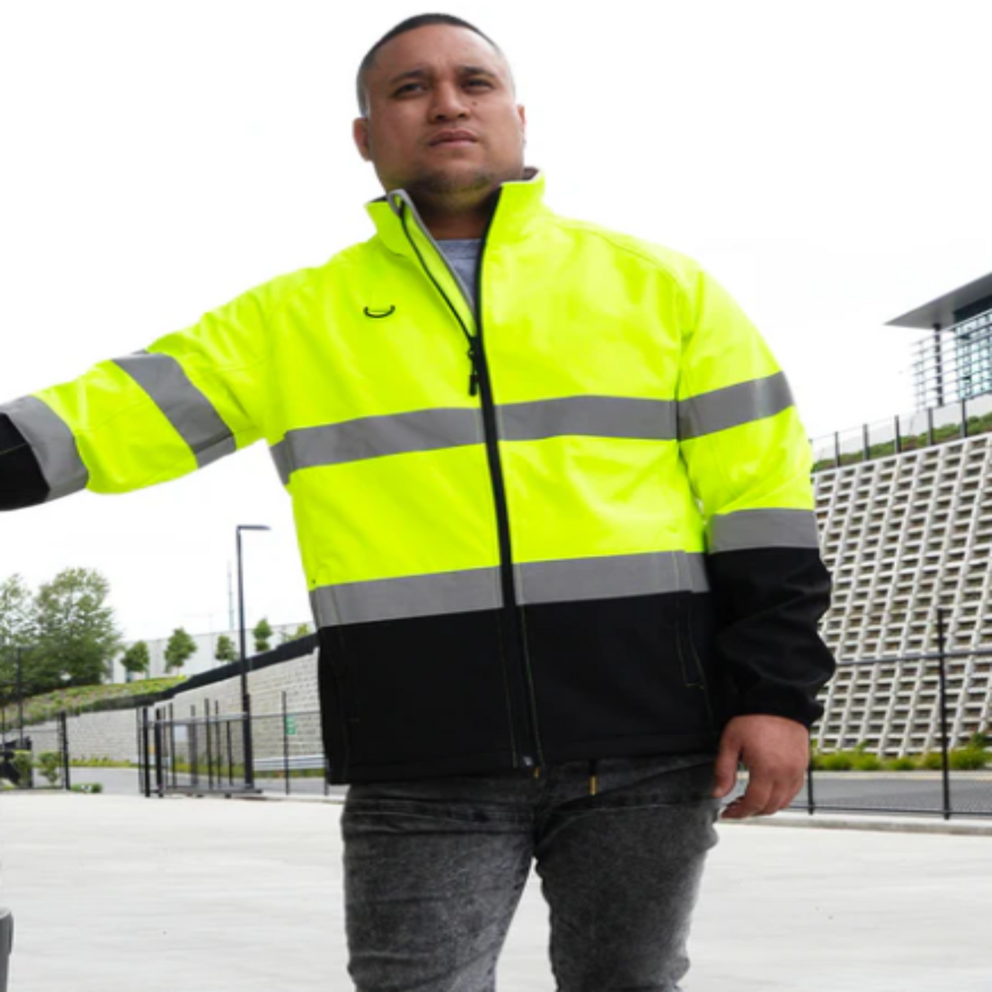 Person wearing a high-visibility jacket with reflective stripes outdoors.