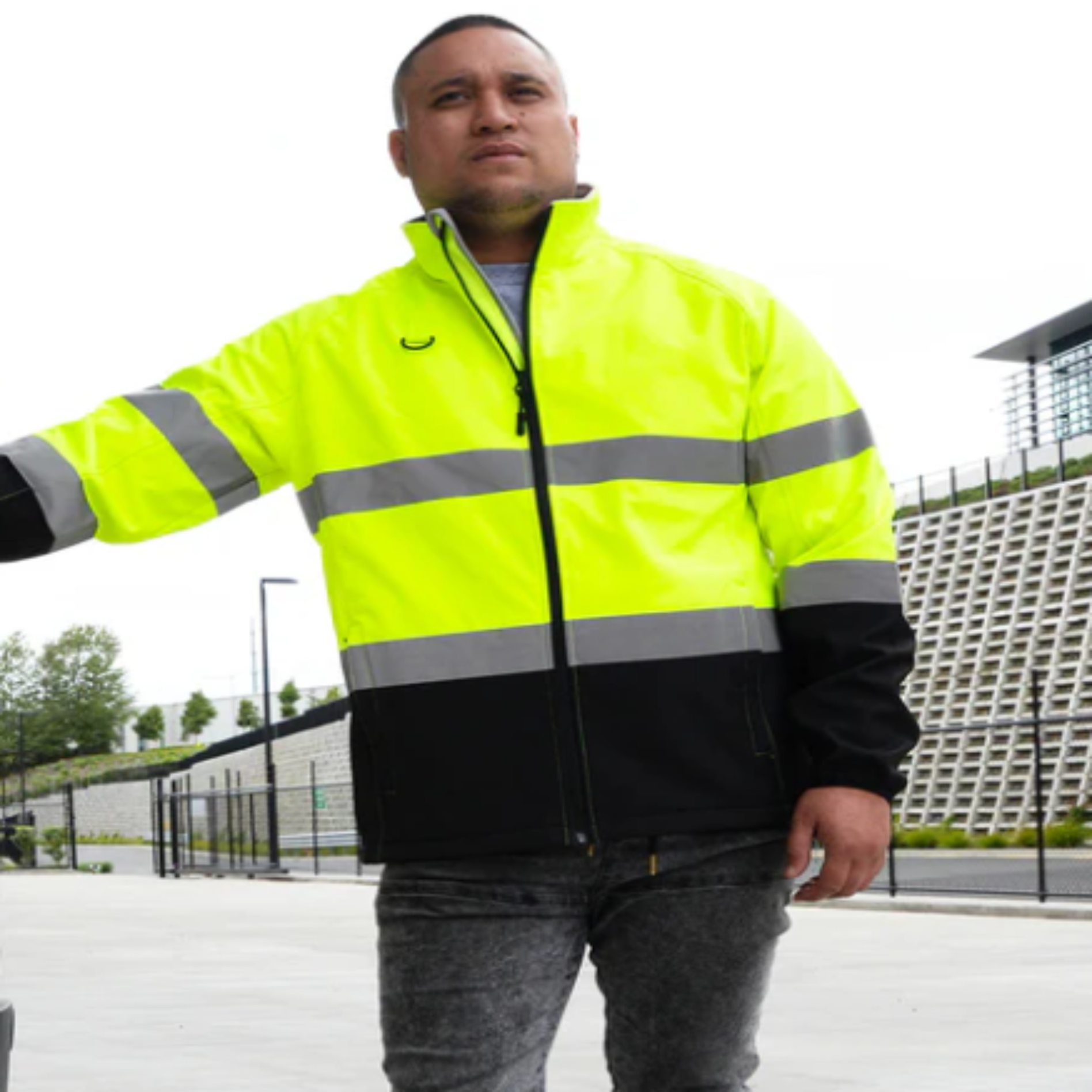 Person wearing a high-visibility jacket with reflective stripes outdoors.
